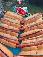Empire Frank plush charm beside a tray of grilled hot dogs at a cookout
