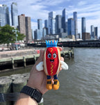 Empire Frank plush charm held up in front of the New York City skyline
