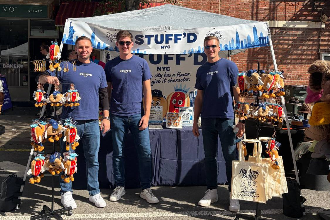 The STUFF'D team at their booth on a New York street, with the plush characters hanging beside them
